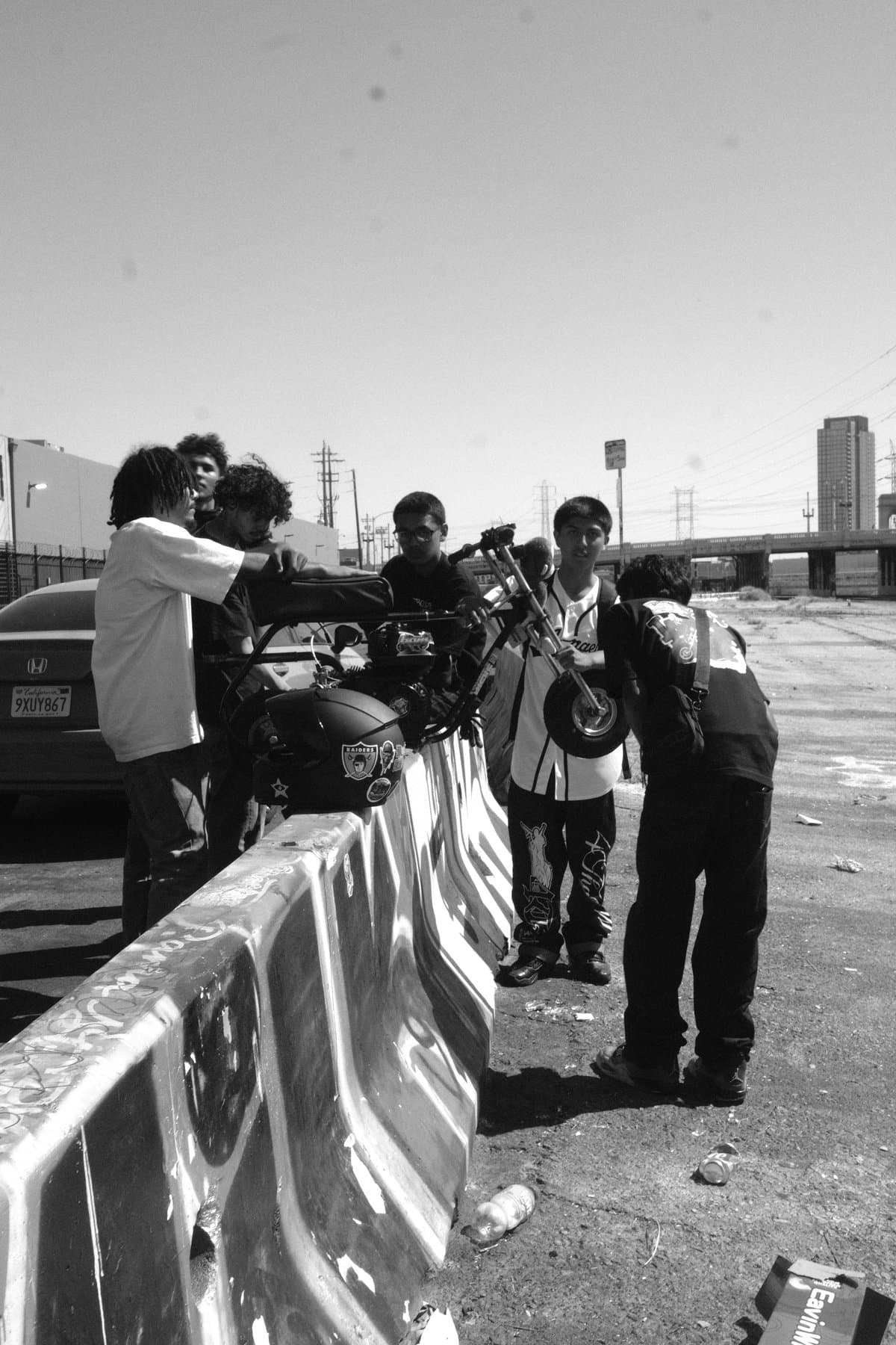 Young men gathered around a minibike on a concrete barrier.